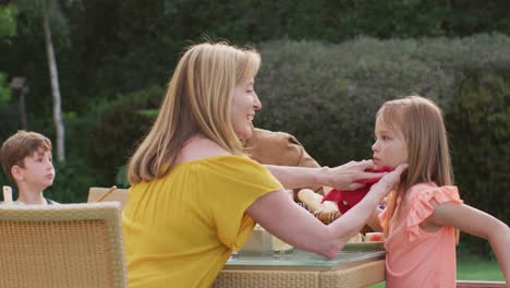 grandmother wiping granddaughter face while having lunch outdoors