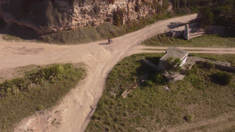 Mountainbiker-riding-on-sandy-path-between-rocks-and-cliffs-during-sunset-in-Argentina