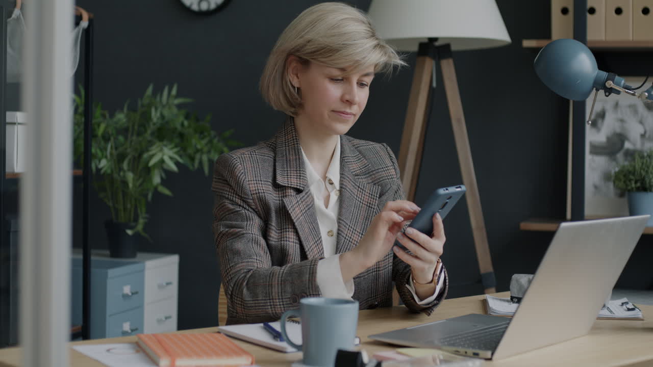Женщина работает в офисе, пользуясь смартфоном