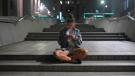 joven usando un teléfono inteligente en las escaleras de la ciudad por la noche
