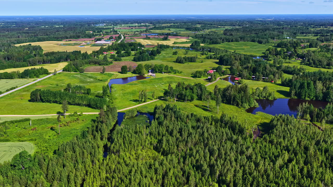 Beautiful and idyllic patchwork landscape of lush green forests, fields, and small ponds in the peaceful Latvian countryside on a sunny summer day - A fast-descending aerial