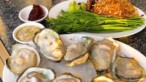 a hand arranges fresh oysters on a bed of ice, surrounded by herbs and sauces.