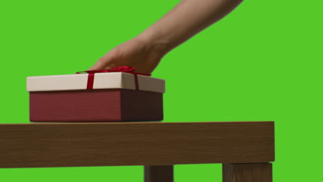 close up of man putting gift wrapped presents onto table shot against green screen