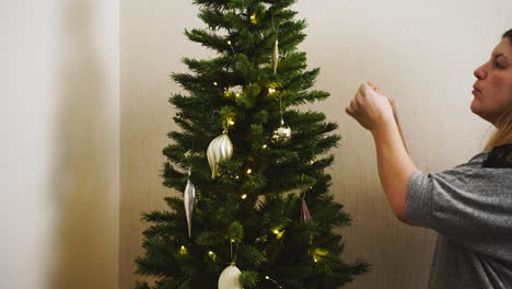 Young-woman-hanging-decorative-glass-ornaments-on-an-artificial-Christmas-tree