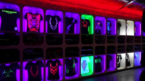 fluorescent graphic t-shirts on a neon-lit wall display at cyberdog store in camden town, london