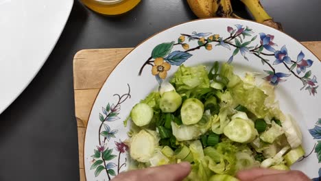 Food-preparation:-placing-cucumber-on-a-plate-with-lettuce-and-purring-oil-on-salad-placed-upon-a-wood-surface