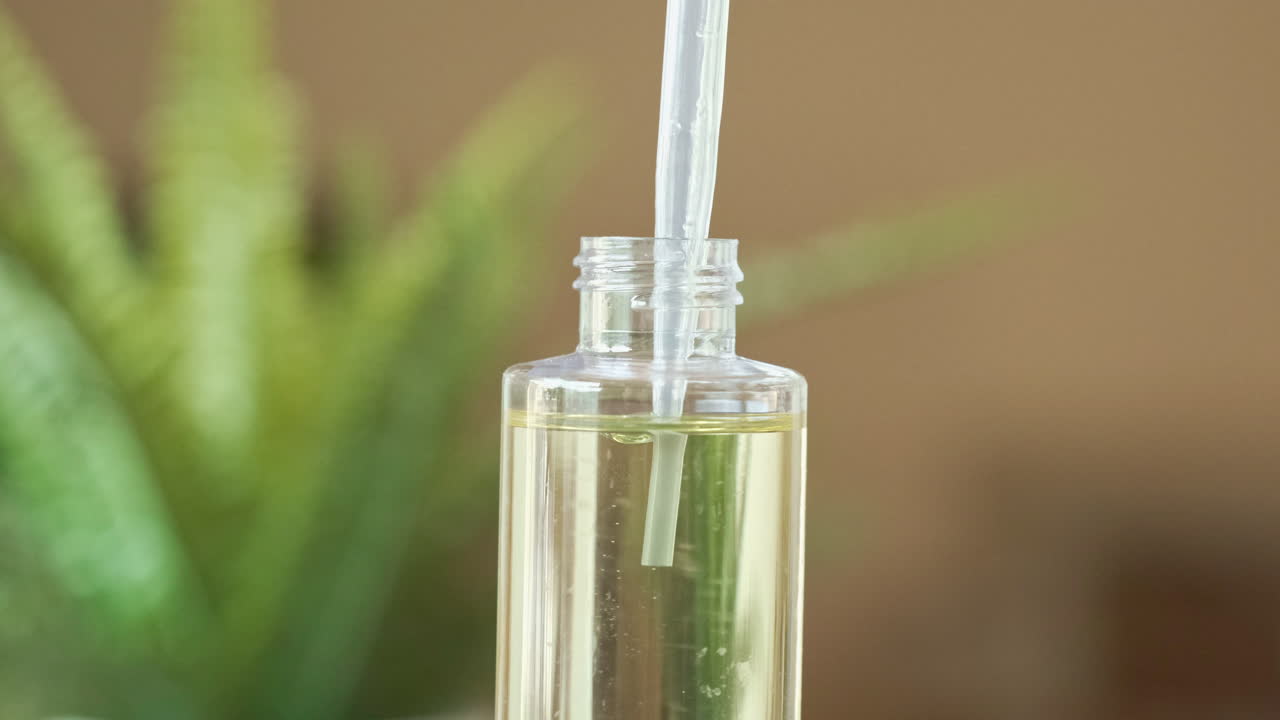 cuentagotas de aceite esencial en cámara lenta exprimiendo gotas de aceite en un recipiente transparente, helecho suave en el fondo, brillante y fresco, día de spa
