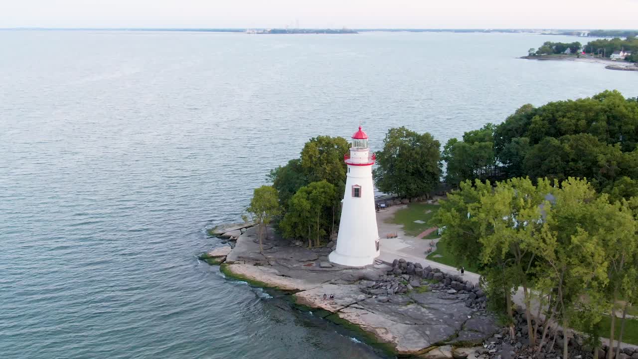 The camera pulls back from Marblehead Lighthouse at sunset, showing visitors on the rocks and Cedar Point in the distance across Sandusky Bay