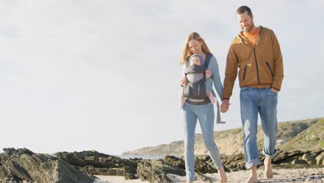 Side-view-of-happy-caucasian-family-walking-at-beach-on-a-sunny-day-4k