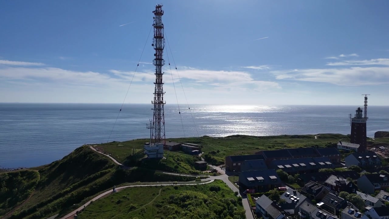 Aerial flight over Unterland houses toward Oberland with lighthouse radio tower and sea.