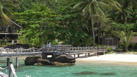 Model-in-a-white-dress-walking-over-a-wooden-bridge-on-a-tropical-island