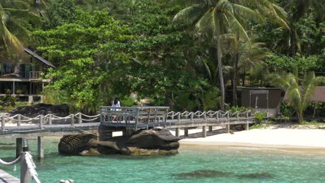 model in a white dress walking over a wooden bridge on a tropical island