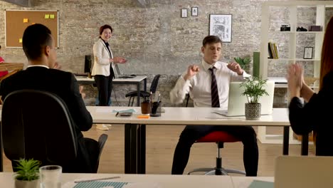 business people of mixed ethnicity in office working and suddenly caucasian man starting cheering and dancing, everyone clapping