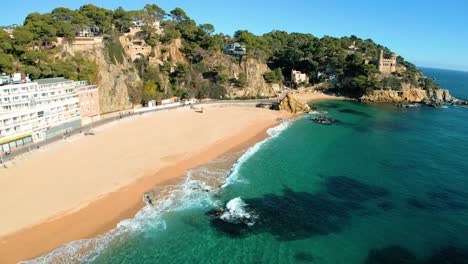 Playa-De-Sa-Caleta-En-Lloret-De-Mar-Castillo-Sobre-Las-Rocas-Joven-Turista-Volando-Con-Drone-Sobre-La-Playa-Principal,-Agua-Azul-Turquesa-Sin-Gente