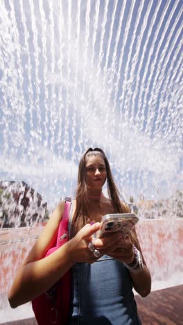 young woman using smartphone under a water fountain
