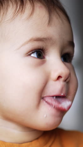 lovely little child being naughty during feeding. boy opens smudged mouth, showing his tongue. close up. vertical video