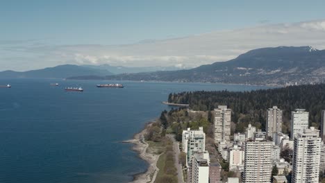 aerial fly over english bay second beach stanley park residential beachside park road as freightors are in the harbor fueling up exports imports on hot summer day suprinsingly quiet traffic and people