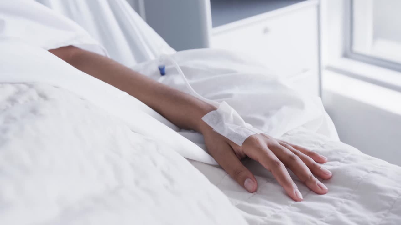 mano de una paciente afroamericana acostada en una cama en una habitación de hospital, cámara lenta