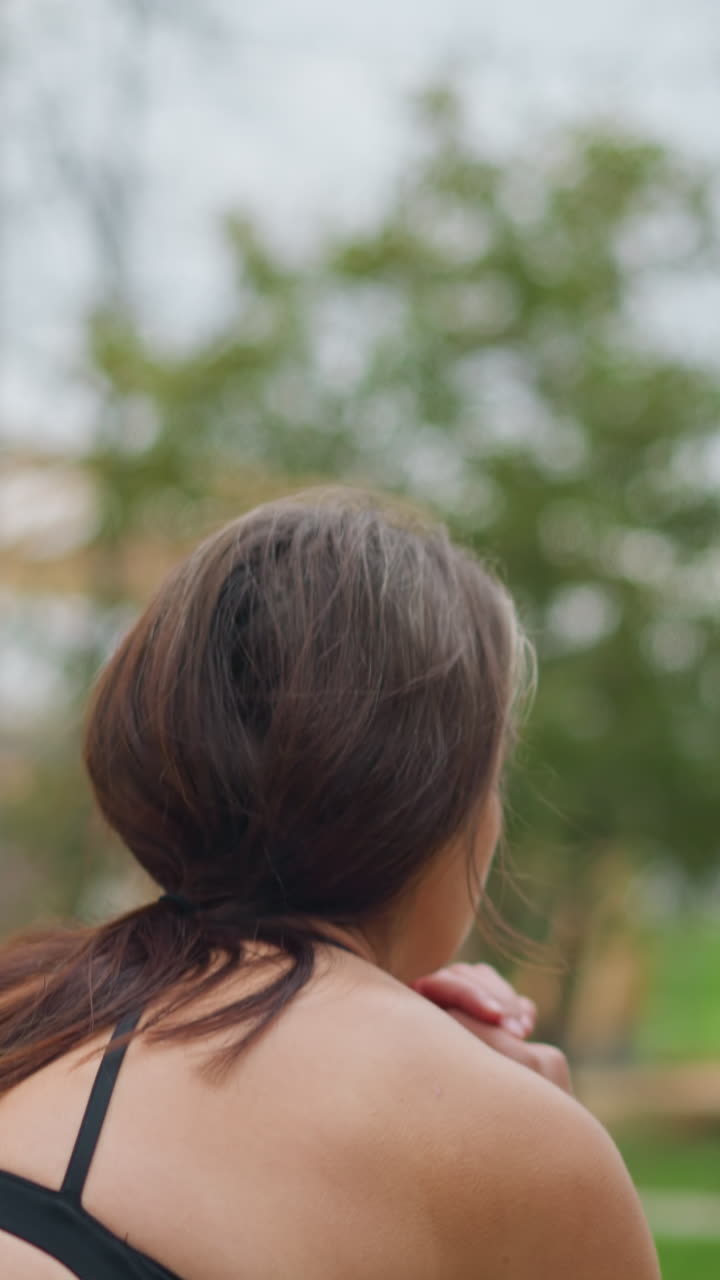 Close-up view of woman in fitness wear squatting down with focus on legs near concrete bench outdoors in park, showing dedication to strength training and fitness routine