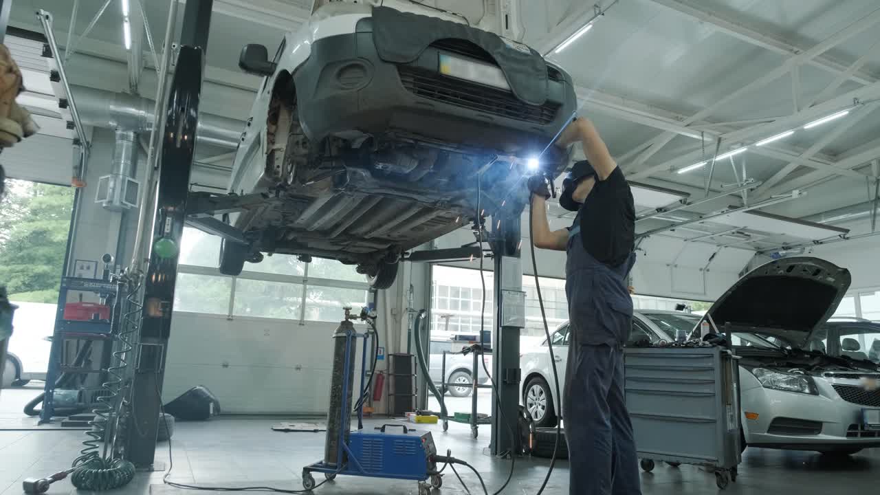 자동차 서비스 노동자는 자동차의 배기가스 파이프를 용접하고 수리합니다. 들어올린 차에 대한 근접 용접 작업. 뒤에서 볼 때. 기계공은 차의 바닥을 용접합니다.