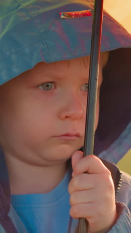 niño bajo una lluvia con las cejas arrugadas. la soledad del niño bajo un paraguas acentuada por la lluvia implacable que proyecta sombra sobre el estado de ánimo. incomodidad palpable