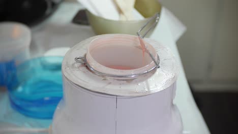 cose up of a beautician preparing for leg waxing by applying wax to a spatula from a wax pot