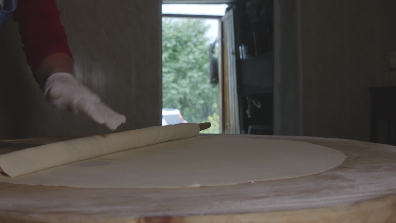 긴 나무 롤링 핀이 있는 베이커는 킨칼리 만두용 반죽을 굴립니다.