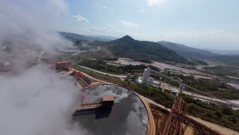 FPV aerial around gold refinery factory with white smoke and large clarifier