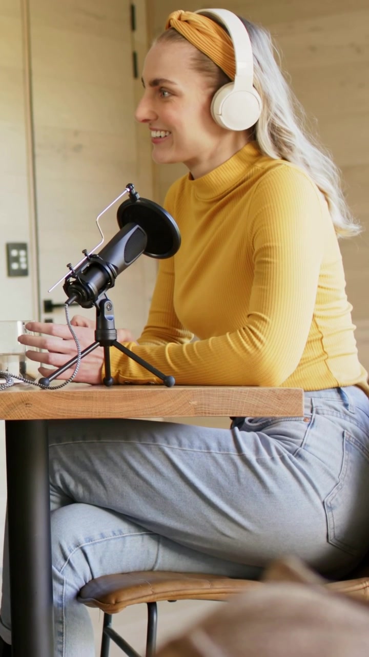 Video verticale: Rispondendo a un segnale fuori campo, una donna con un top color senape e cuffie parla al microfono in studio.