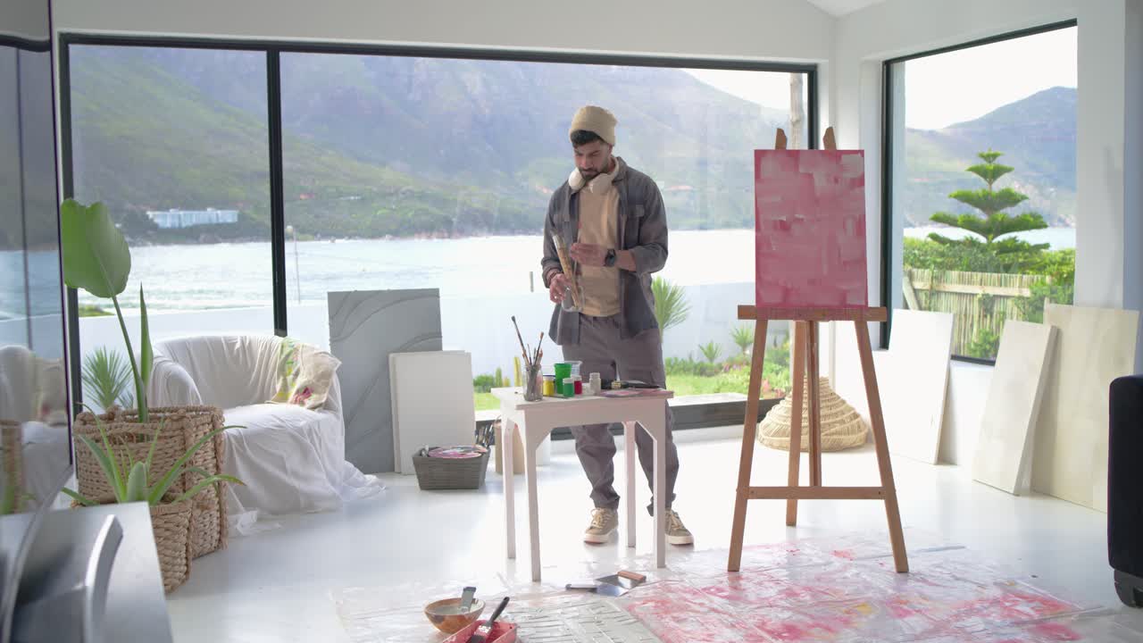 Indisk mand i et studie føler sig inspireret af en sø, går hen til et bord, blander farve, maler et lyserødt lærred