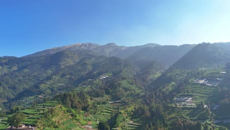 a drone view of a lush tropical mountain bathed in morning sunlight, showing streaks of sunlight piercing the thin mist. mount merbabu, indonesia