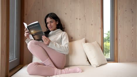woman relaxing at home, reading book by window on cozy day, copy space