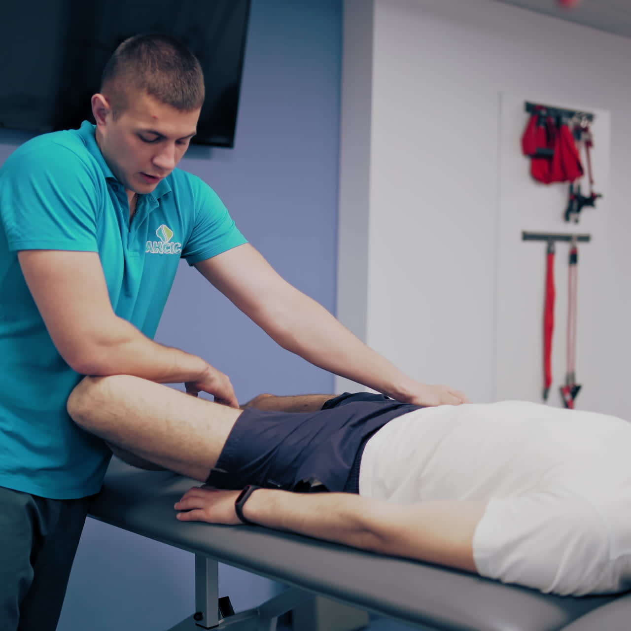 Therapist is doing massage and stretching leg to a male patient in clinic. Physiotherapist is giving leg treatment to a client lying on a massage table in rehabilitation center. Physical therapy concept.