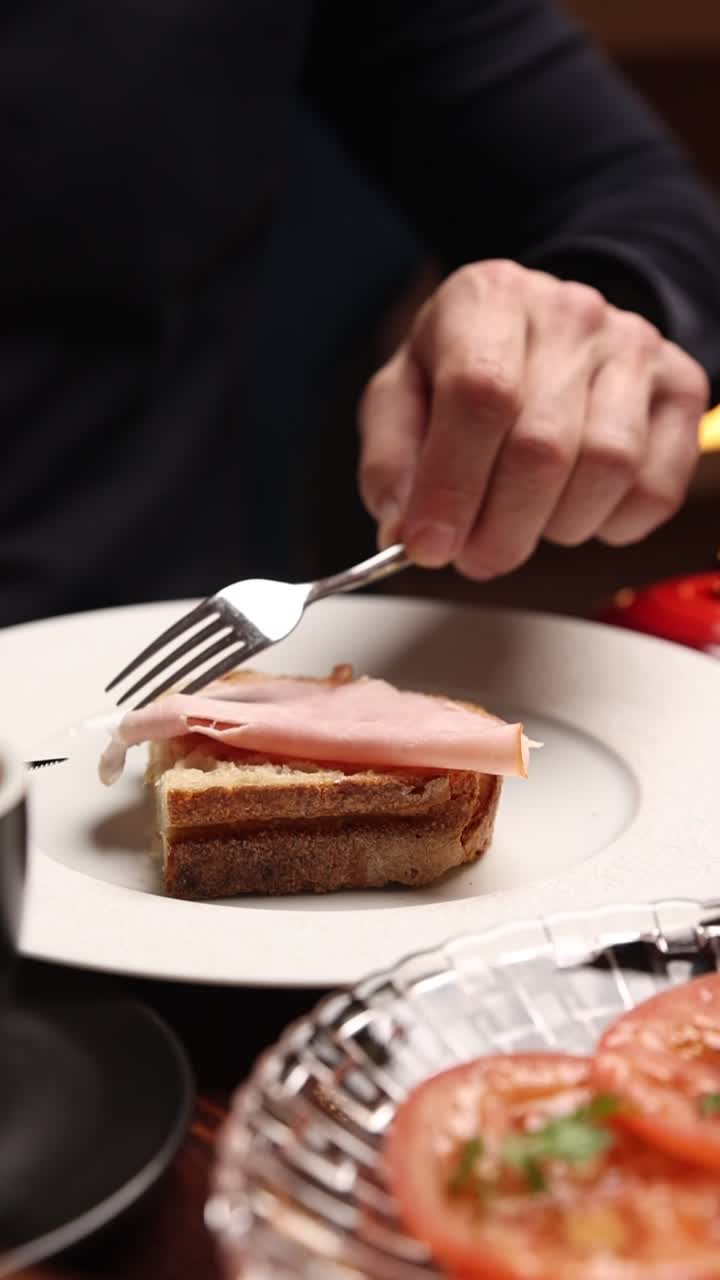 Detail ruky pokládající šunku na topinku vidličkou