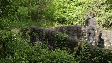 Mann-Blickt-über-Die-Brücke,-Während-Er-An-Einem-Sonnigen-Tag-Im-Wald-Im-Freien-Spazieren-Geht---Zeitlupe