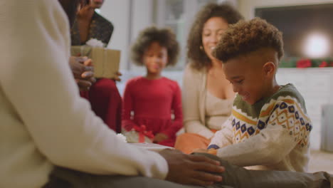 multi-generation family exchanging and opening gifts around christmas tree at home