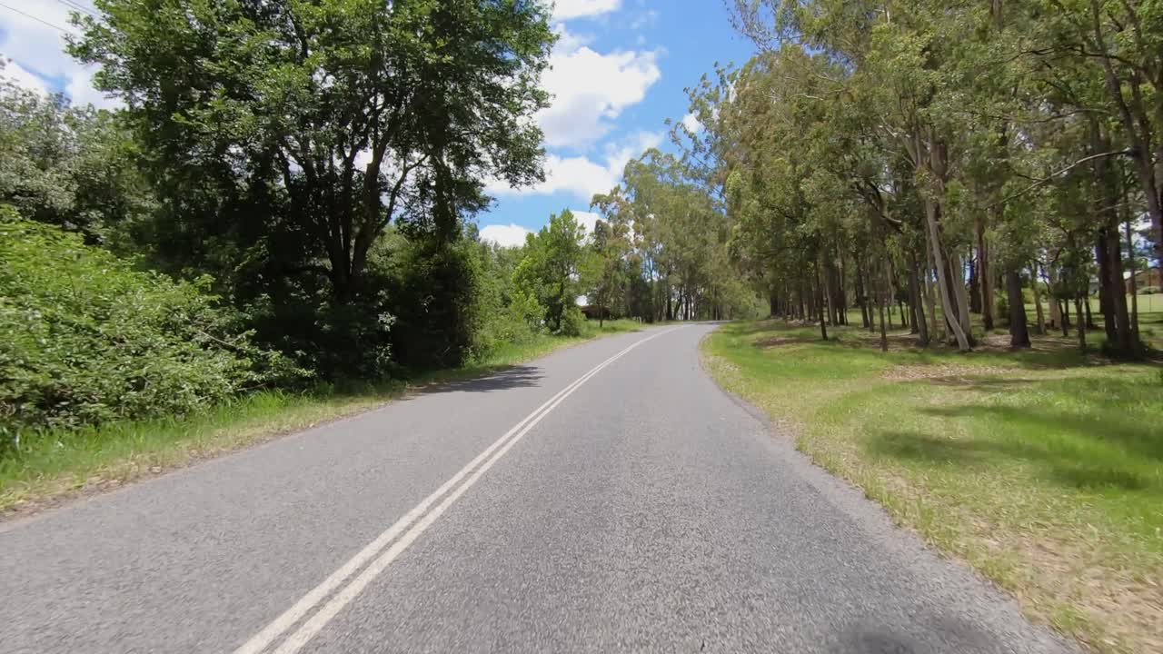 Rear facing driving point of view POV of a deserted Queensland country road with tall trees and hill ascent - ideal for interior car scene green screen replacement