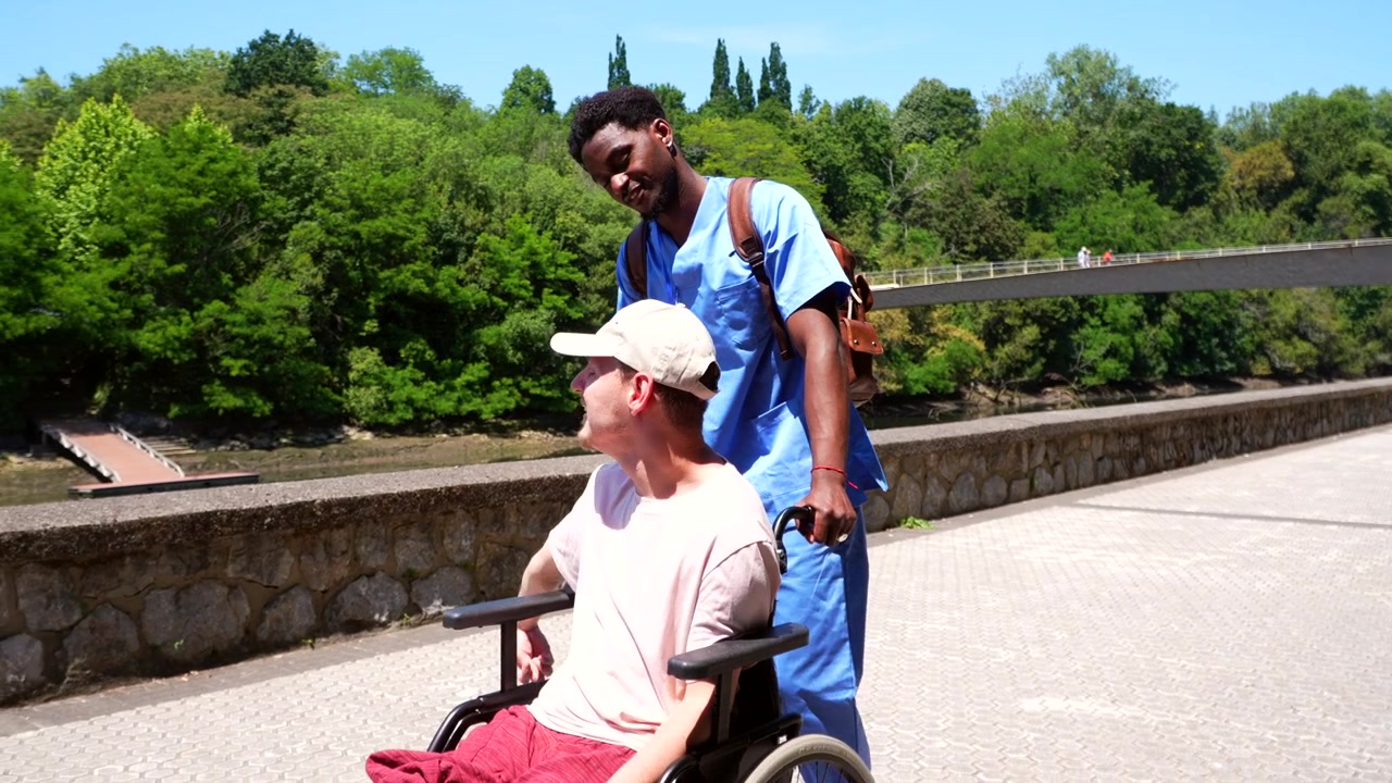 Aidant poussant un jeune homme en fauteuil roulant en extérieur