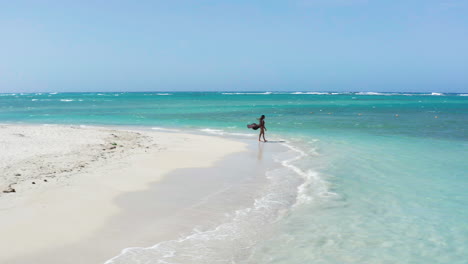 Cinematic-drone-shot-of-single-woman-tourist-on-beach,-wind-blowing-sarong,-pristine-waves-and-water