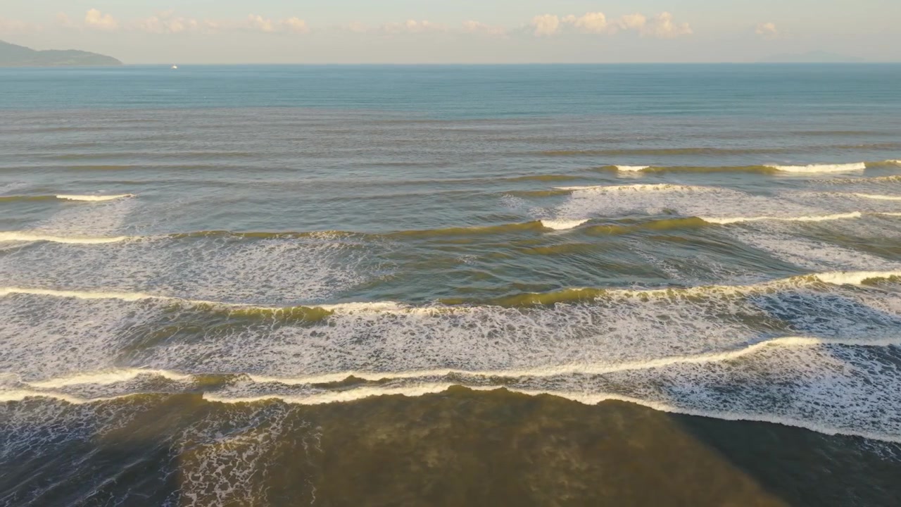 Vietnam, Da Nang. Lunghe onde si infrangono lungo la costa di Da Nang, con onde stratificate e schiuma testurizzata sotto un cielo sereno. Vista aerea panoramica che cattura motivi e movimento, ideale per contenuti di viaggio ed editoriali.