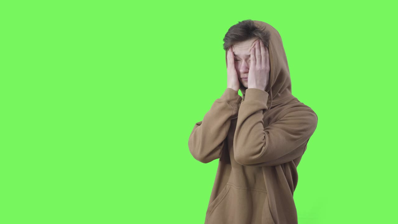 Adolescente caucasico disperato si strofina le tempie e sospira. Mezzo busto di ragazzo triste con felpa con cappuccio in posa su sfondo verde. Stress, adolescenza, problema, stile di vita. Chroma key
