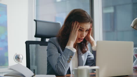 una mujer desesperada, gerente de una computadora portátil, conmocionada por la pérdida de negocios de la oficina de cerca.