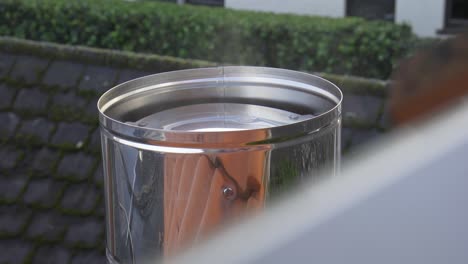 Smoke-coming-from-modern-aluminium-chimney-with-the-rooftop-and-garden-in-the-background