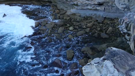 ocean waves washing on big rocks in shoreline of rocky hills