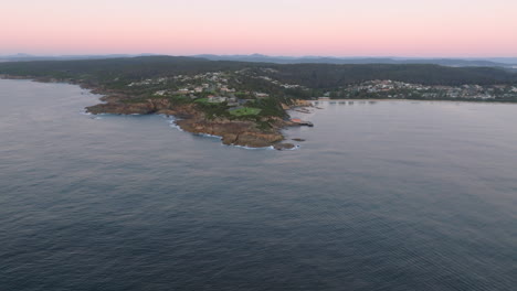 aerial: drone flying from the ocean over tahtra headland, over the town and up the beach, south coast nsw, australia