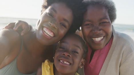 Portrait-of-happy-african-american-grandmother,-mother-and-daughter-smiling-at-beach,-in-slow-motion