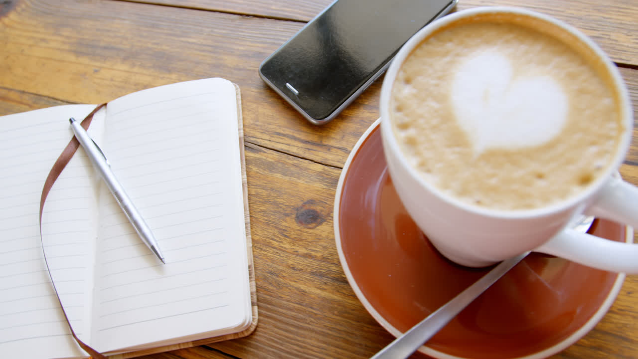 Tazza di caffè latte caldo con latte art a forma di cuore, con un diario e un telefono cellulare 4k
