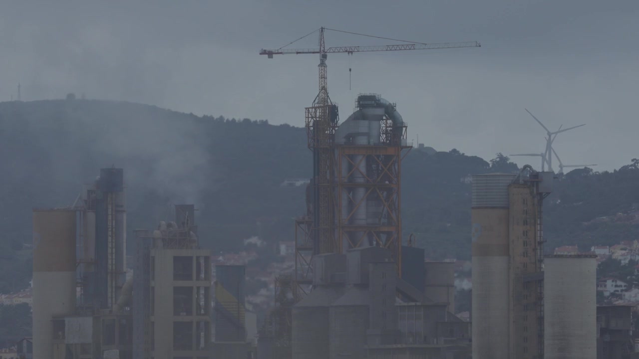 Fabbriche e ciminiere, con impianti industriali in costruzione e gru.