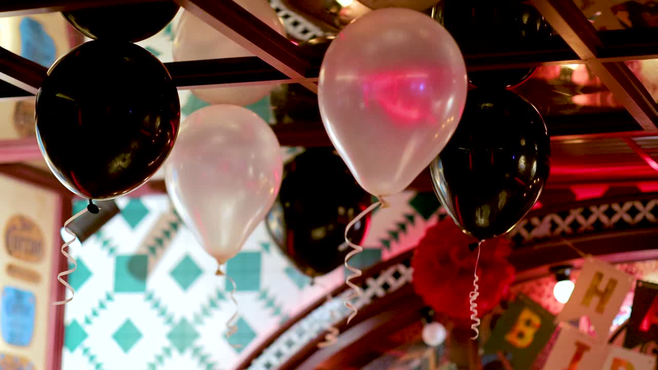 Colorful balloons and birthday banner in warmly lit restaurant, slight camera pan reveals festive decor