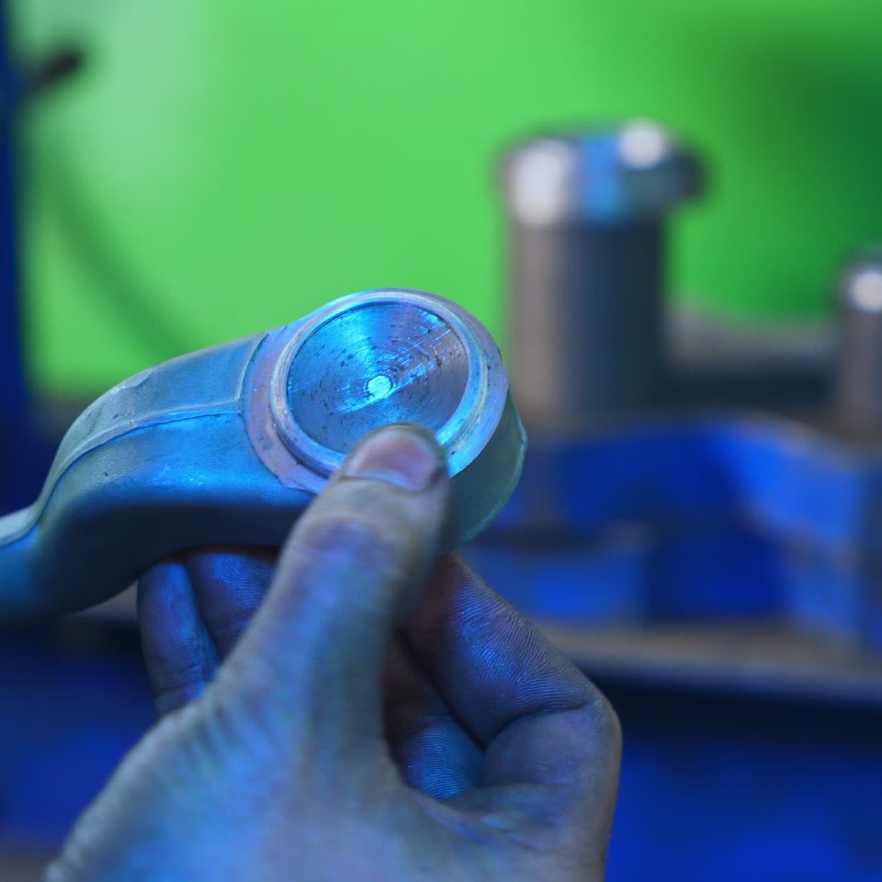 Turner is taking a metal detail and checking it with his fingers. Metal tools and machines at the background in blur